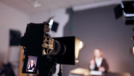 camera recording a female blogger in the studio. little display depicts a woman with long brown hair. close up. blurred backdrop.