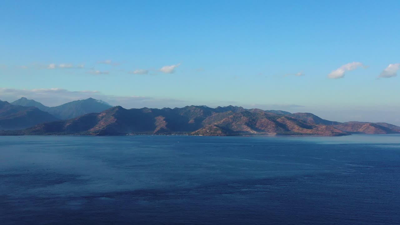 Sunlight shining mountains of tropical islands surrounded by calm surface of blue sea under bright sky with white clouds, Indonesia