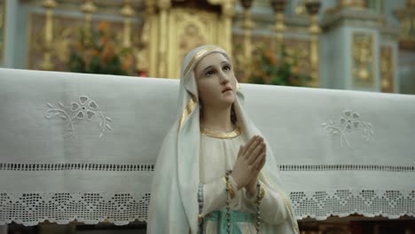 close up of virgin mary statue with folded hands and rosary before ornate altar