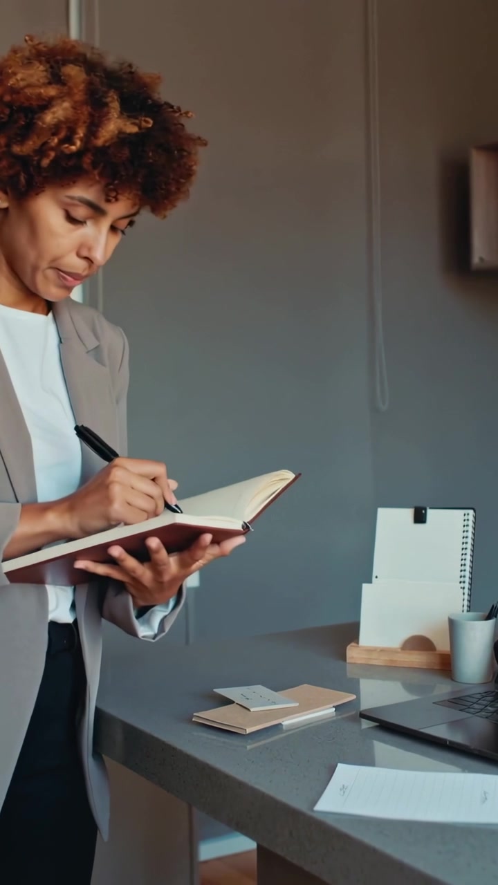 Vertical video: Opening notebook woman blazer-clad flipping pages noting info at desk with pen