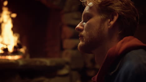 Thoughtful-man-sit-fireplace-in-vacation-house.-Redhead-guy-looking-away-at-home