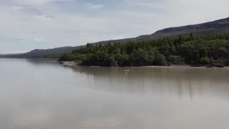 Standup-Paddleboarder,-Der-Friedlich-Am-Waldufer-Des-Flusses-Lagarfljot-Vorbeischwebt