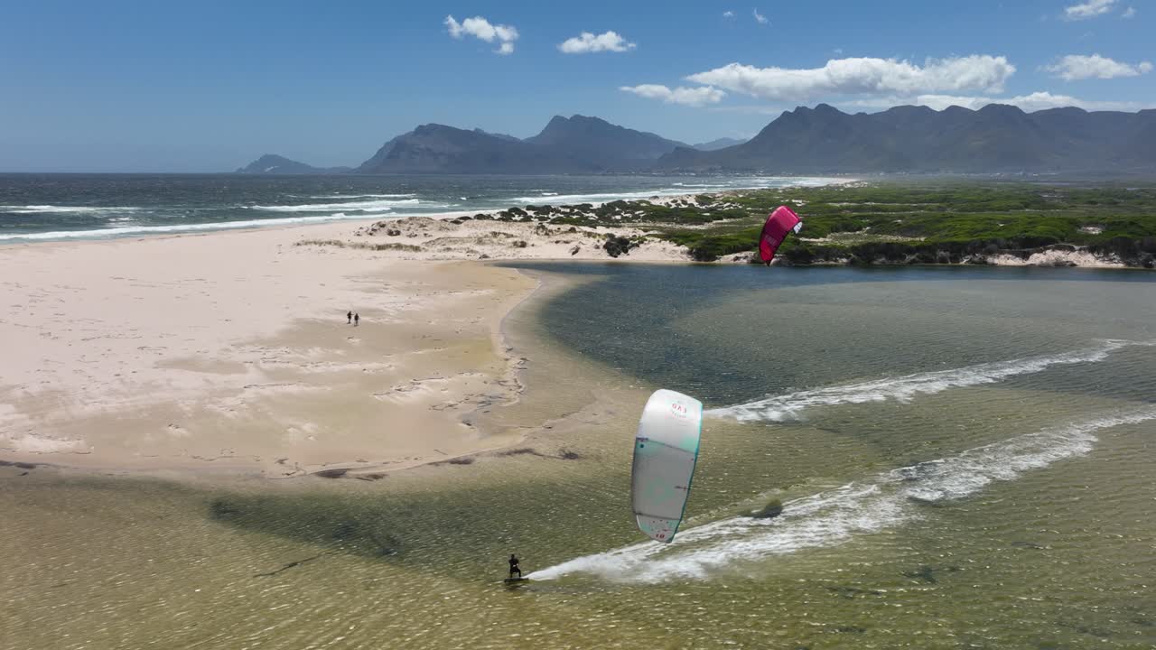 toma aérea de dos kitesurfistas en la laguna de hermanus haciendo trucos