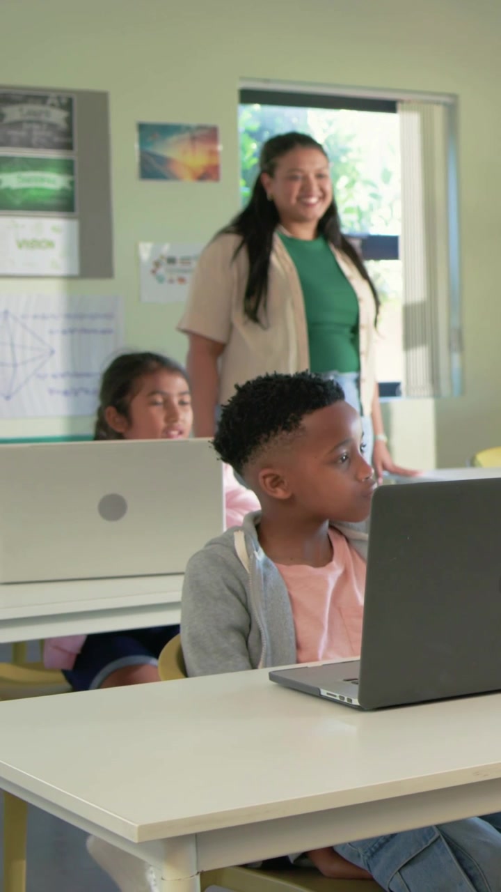 Video verticale: Un ragazzo in primo piano, al laptop in classe per la lezione, reagisce all'ingresso dell'insegnante con una maglietta verde.