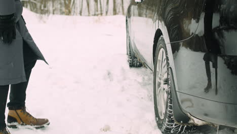 el primer plano de un hombre irreconocible revisando las ruedas de un auto durante un día de invierno con nieve