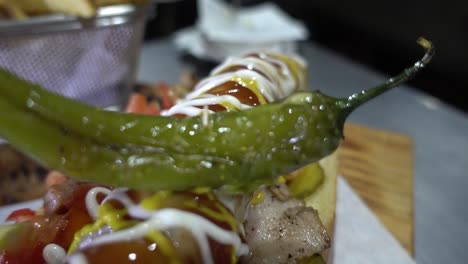 slow revealing shot of a hotdog covered with different sauces and a jalapeno