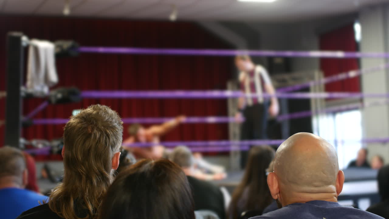 un árbitro de lucha cuenta el pinfall mientras la audiencia mira atentamente, su enfoque en la acción dentro del ring