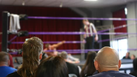 a wrestling referee counts the pinfall as the audience watches intently, their focus on the action inside the ring