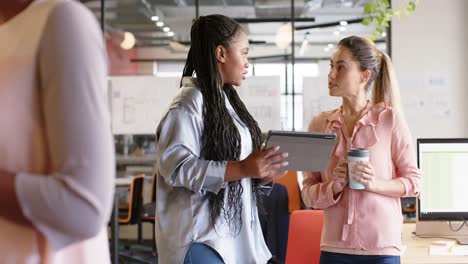 Diverse-businesswomen-discussing-work-and-using-tablet-at-office,-in-slow-motion