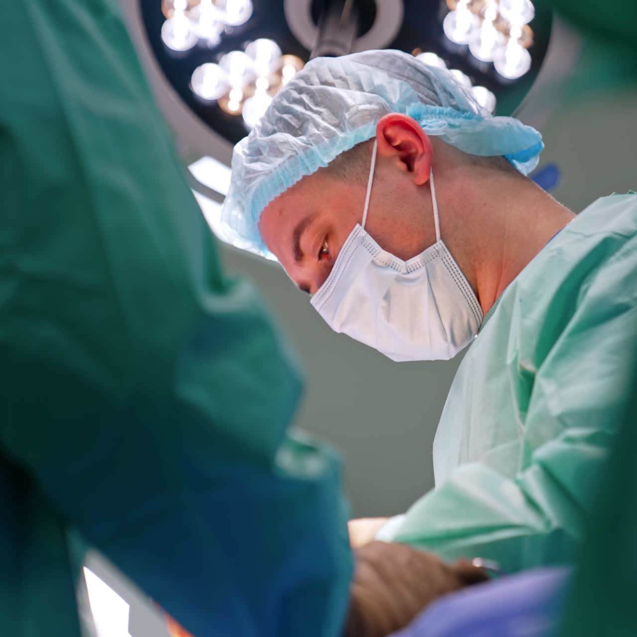 Sguardo concentrato di un chirurgo con mascherina che guarda il paziente. Ritratto di profilo di un medico che lavora a un intervento. Vista dal basso.