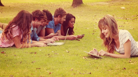 Pretty-blonde-using-tablet-in-the-park-with-friends-behind