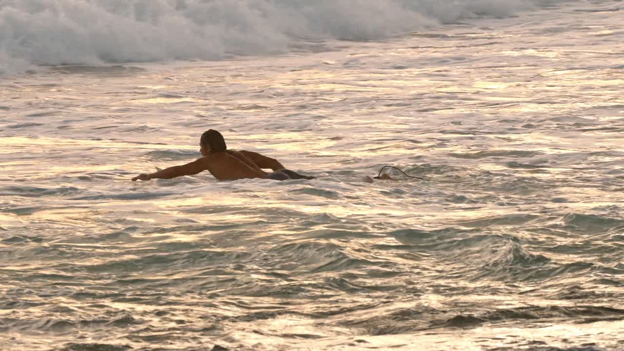 A serene moment of a surfer paddling in the warm waters of Weligama at sunset. The golden light reflects off the ocean, creating a peaceful and cinematic scene.