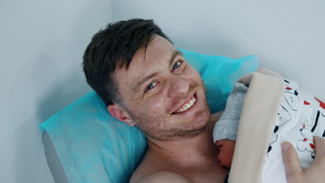 happy caucasian man is excited to hold his newborn baby. father is having tears in his eyes holding his child carefully. top view.