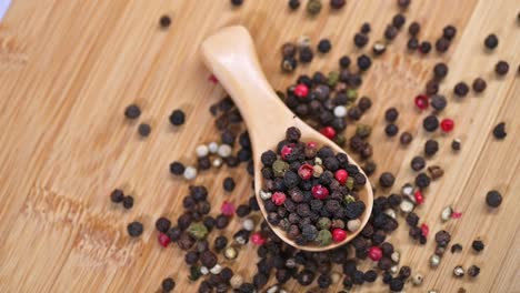 a wooden spoon filled with a colorful mix of black, red, green, and white peppercorns rests on a wooden cutting board. scattered peppercorns create a rustic and natural culinary setting.
