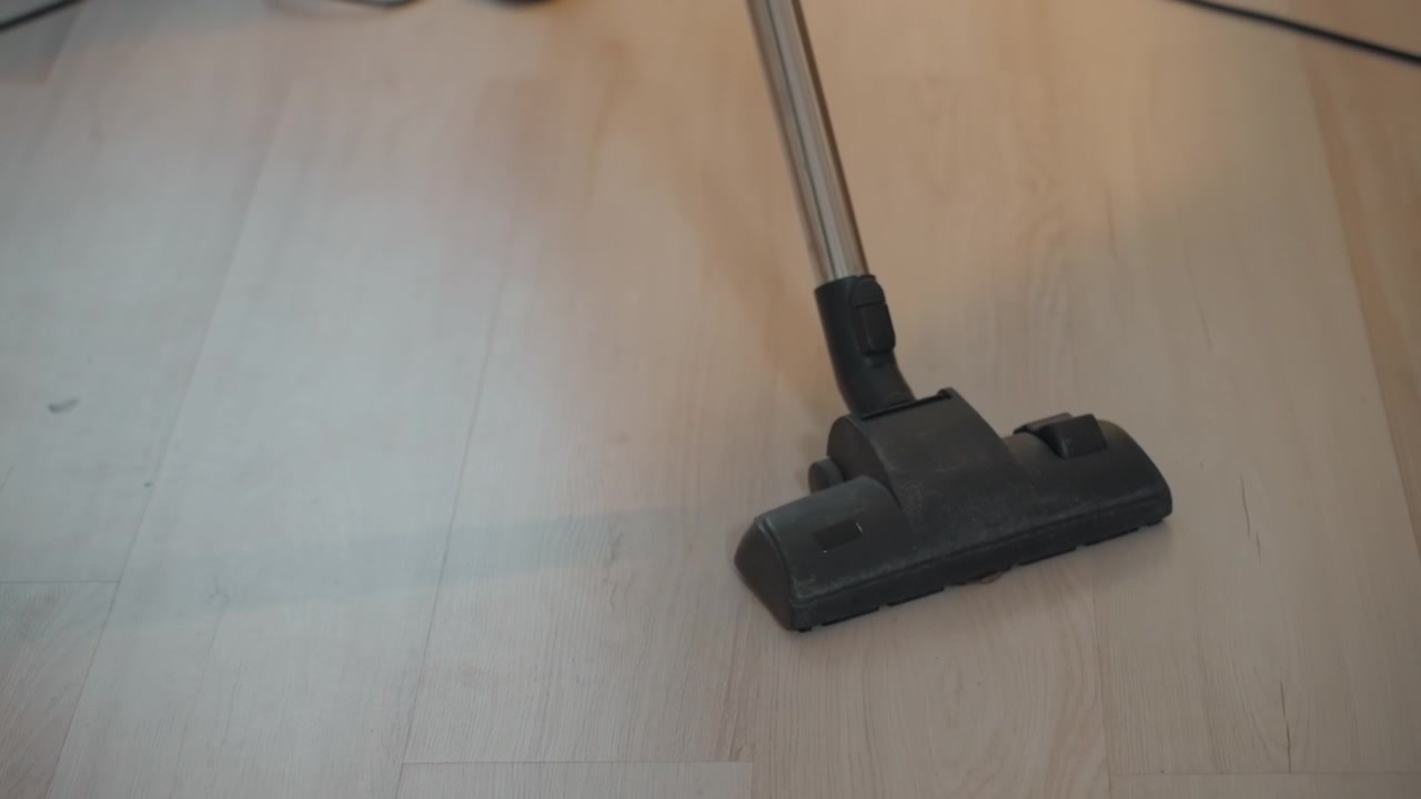 Vacuum head glides over laminate floor, soft natural light, minimal dust particles lifted, steady backandforth motion, closeup of nozzle and handle, cord trailing across room, warm home atmosphere