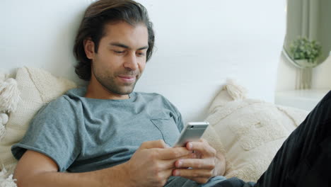 Man Relaxing on Bed and Using Smartphone