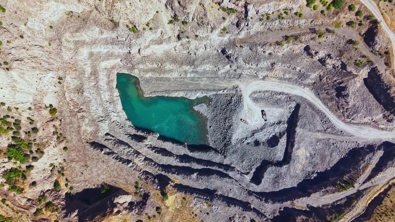 View of a quarry showing steep rock walls and a small body of green water at the bottom surrounded by gray and brown earth in a remote area
