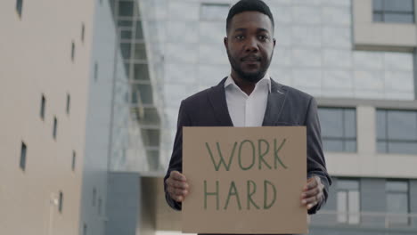 man holding sign that says "work hard"