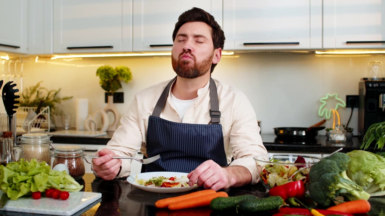 Mann mittleren Alters genießt frischen Gemüsesalat in der heimischen Küche als vegetarisches Abnehm-Mittagessen