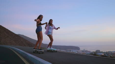 two friends donning shorts engage in slow-motion skateboarding along a road at sunset, with mountains and a captivating sky in view