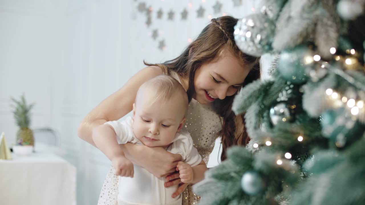primer plano niña feliz sosteniendo a un niño cerca del árbol de navidad en una casa moderna.