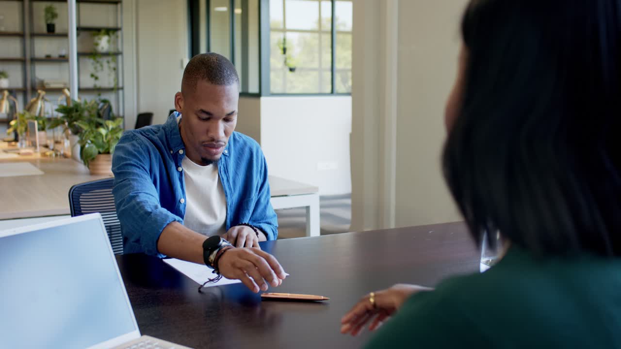 Staff member sliding form to client at office table, man taking pencil and signing for application