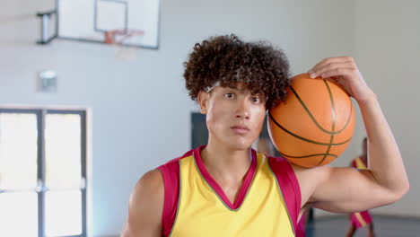 young biracial man poses in a basketball court