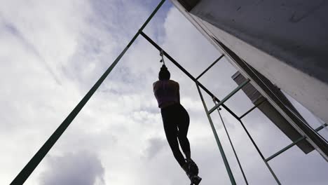 dynamic slow motion footage of a fit woman succeeding at reaching the top while climbing a rope, backlit against the clouded sky