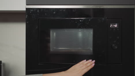 female hands put plate with dish in built-in microwave oven