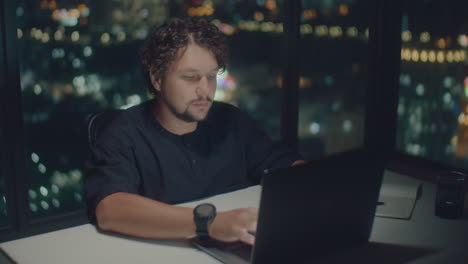 curly-haired man typing text at a computer at night