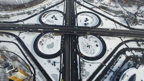 Drohnenansicht-Eines-Autos,-Das-Sich-Auf-Der-Autobahnkreuzung-In-Der-Winterstadt-Bewegt.-Verschneite-Stadtlandschaft