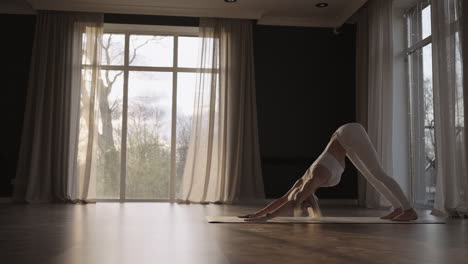 A-young-woman-in-a-white-suit-in-a-gym-trains-yoga-in-the-sun-in-slow-motion