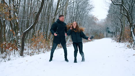 caucasian people jumping happily in winter park. a couple wearing warm clothes cheering excitedly.