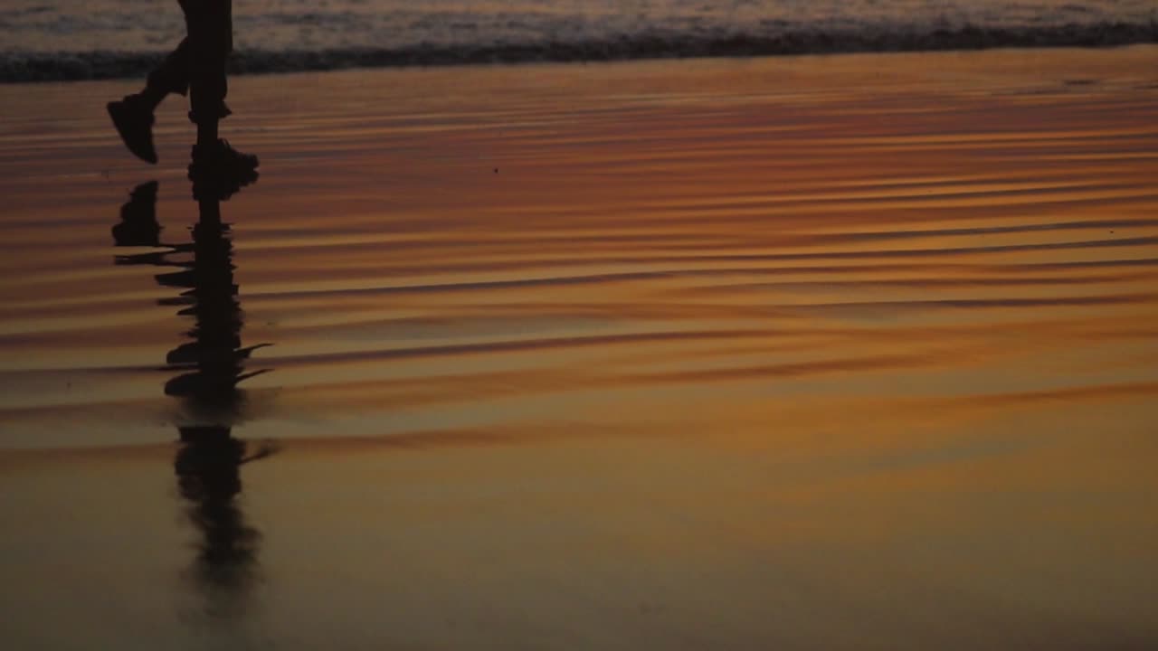 Close look on boy's legs silhouette walking on the sandy beach near the sea early in the morning