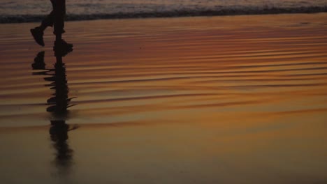 Close-look-on-boy's-legs-silhouette-walking-on-the-sandy-beach-near-the-sea-early-in-the-morning