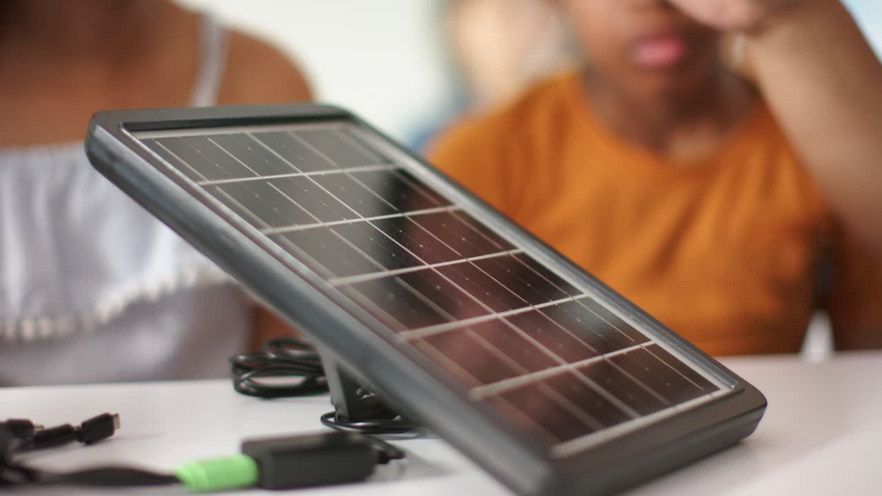 Bambini afroamericani curiosi testano un pannello solare su un tavolo, controllando una spina verde a scopo didattico.