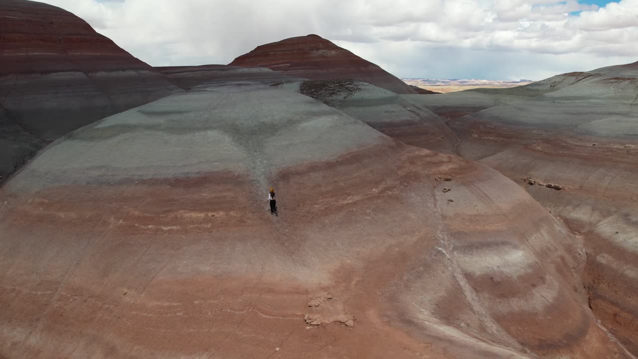 Vista aerea di una donna che corre da sola verso la cima di una collina con strati di arenaria, ripresa con drone.