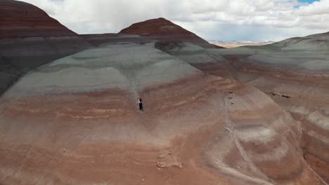 vista aérea de una mujer corriendo sola a la cima de la colina con capas de piedra arenisca, disparo de avión no tripulado