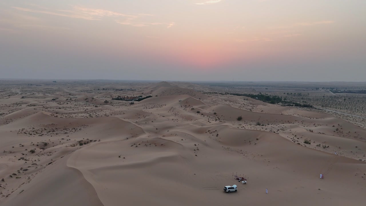 Desert sand dunes with small vehicle crossing sandy terrain at sunset in Abu Dhabi, aerial dolly