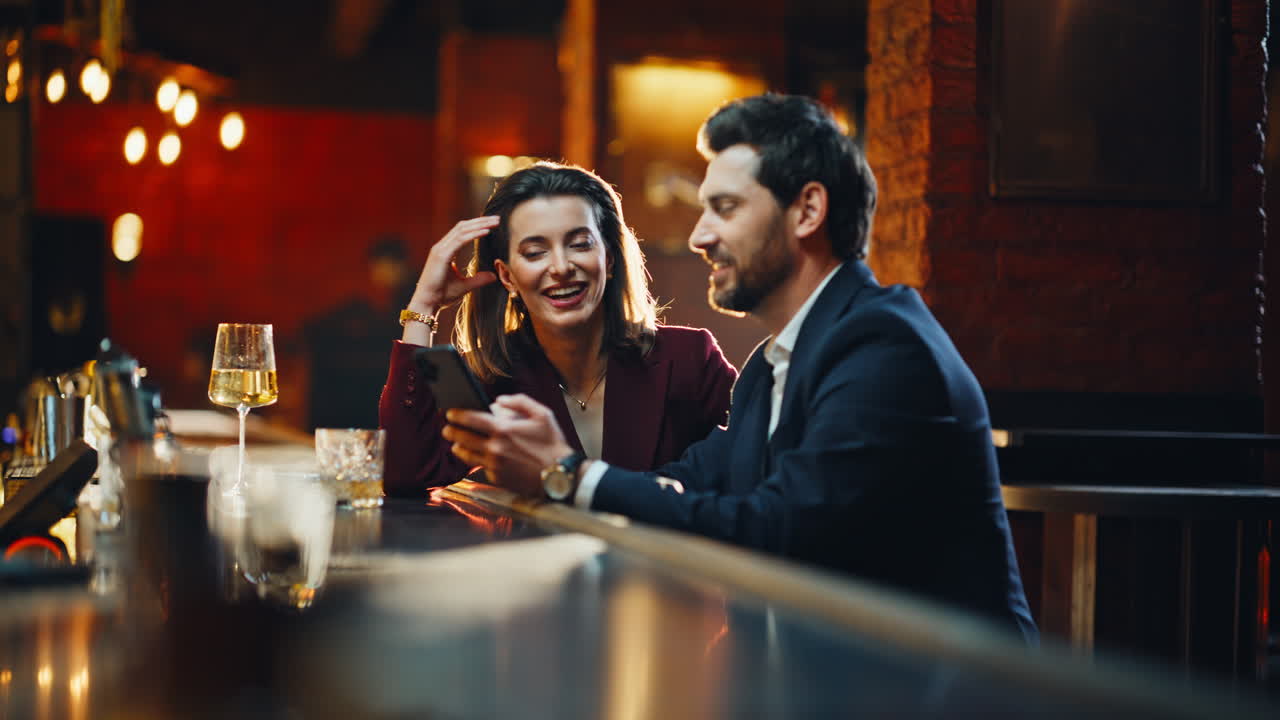Uomo e donna si rilassano insieme in un bar di notte, mentre parlano usando uno smartphone. Coppia felice