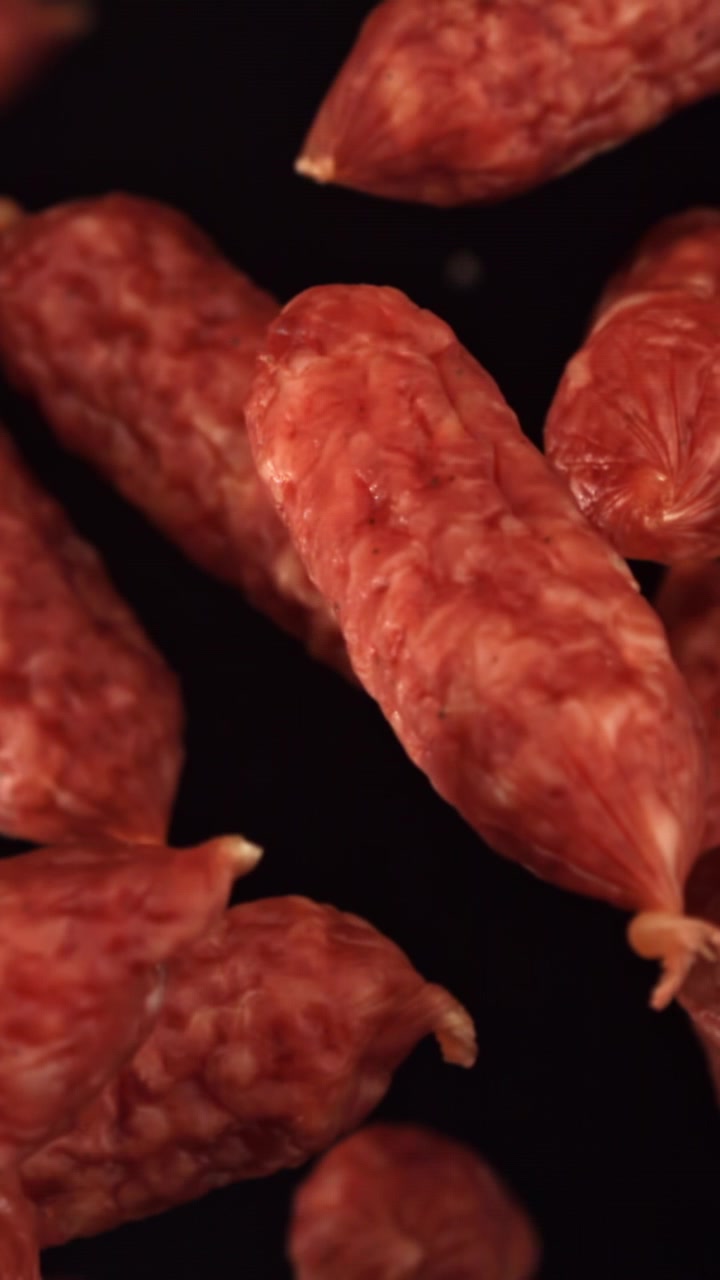 Mini salsicce di salame che cadono al rallentatore su sfondo nero.