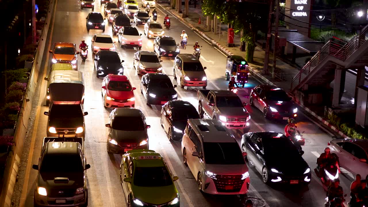 Overhead view of congested city street with cars, motorcycles, and bright streetlights at night