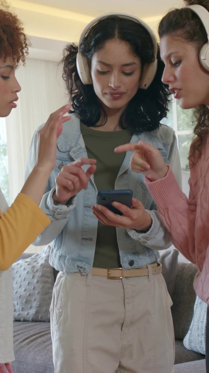 Vertical video: Holding phone, trio with headphones scrolling and choosing at home, denim jacket