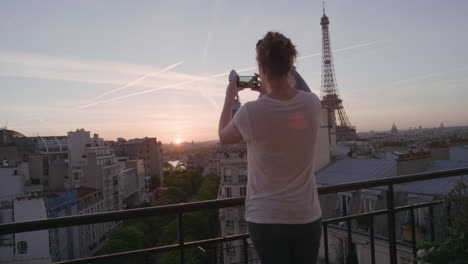 mujer feliz usando un teléfono inteligente tomando fotos disfrutando de compartir la experiencia de las vacaciones de verano en parís fotografiando la hermosa vista del atardecer de la torre eiffel en el balcón