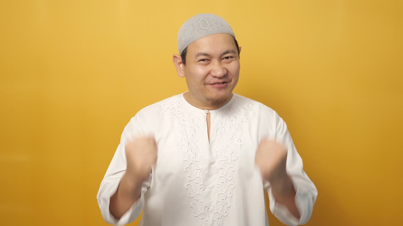 Menestyksekäs onnellinen muslimimies huutaa ja osoittaa voiton elettä keltaista taustaa vasten