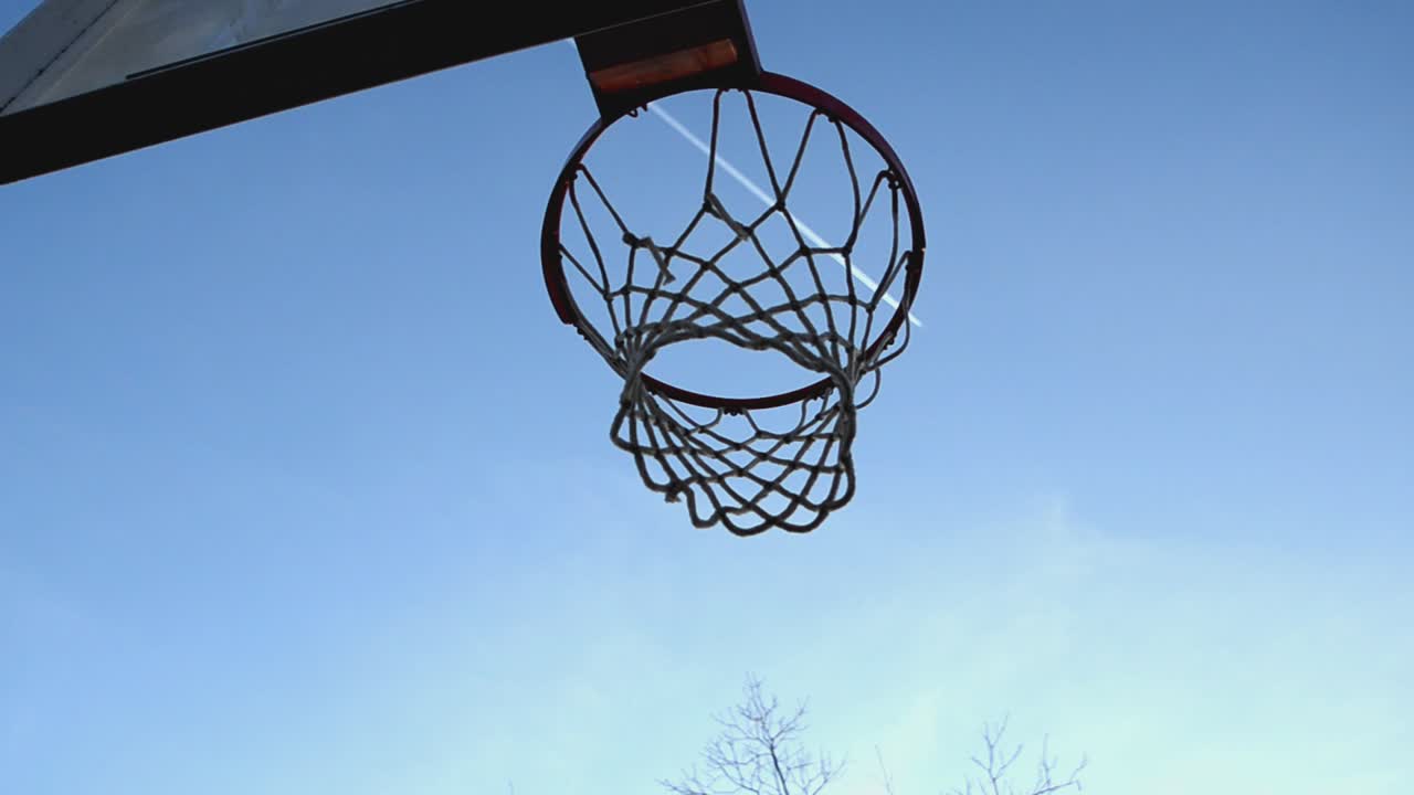una vista desde debajo de un tablero de baloncesto y una red con un cielo azul y un avión volando por el horizonte