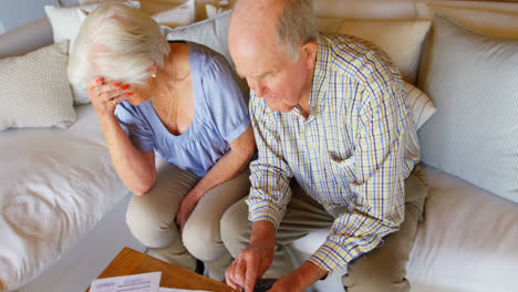 high angle view of old caucasian senior couple discussing over bills in living room at comfortable h