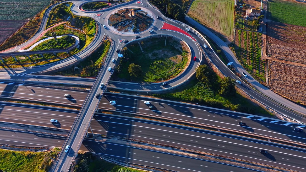 Multilane highway with overpass and roundabouts at dusk, Spain. Aerial drone view of converging roads, vehicles and green landscape.