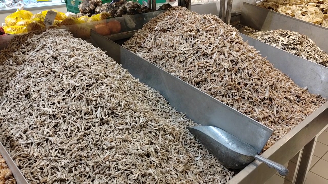 Various types of anchovies are displayed in bulk at a supermarket. They are sorted by quality and size for easy selection. Customers choose their preferred grade before weighing their purchase.