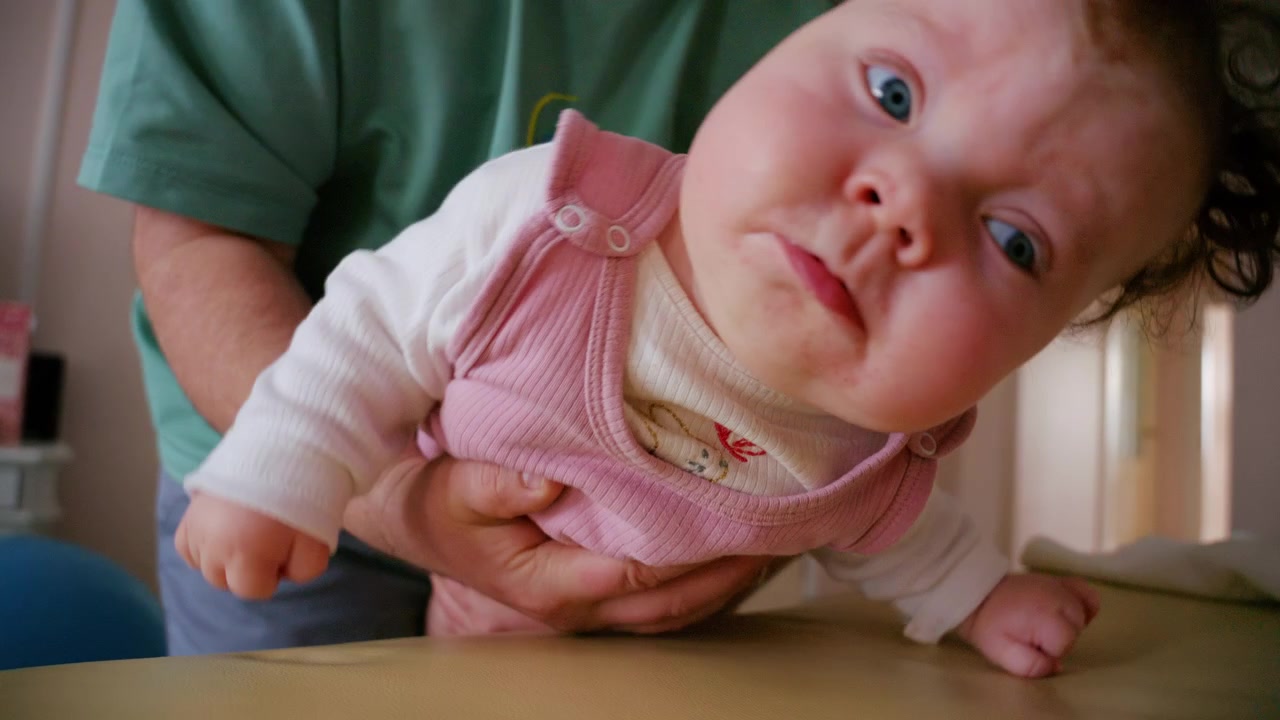 Close up footage of a caregiver gently caring for an infant lying on a cushioned changing mat indoors